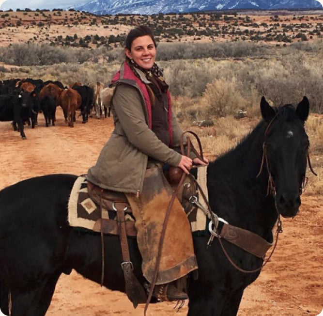 Dr. Joy Moffett-Hatcher on horseback moving cattle across open range