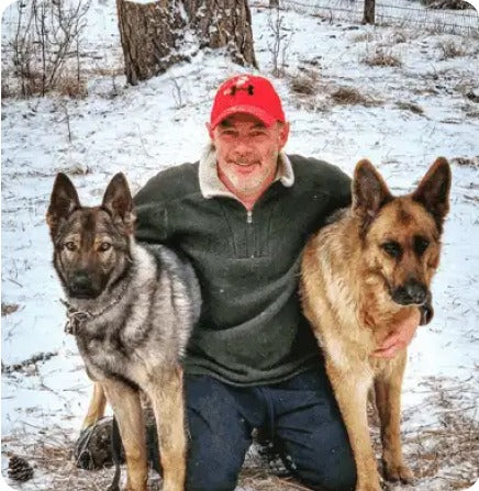 Rick Moffett kneeling in a river with two German Shepherds