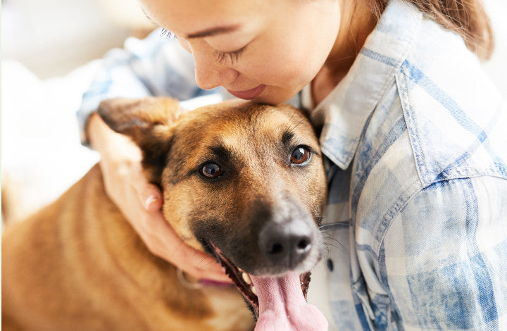 A woman leaning in to hug her tan dog